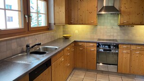 A kitchen with wooden cabinets, a stainless steel sink, a dishwasher, and a stove. - Haus Ares (Zermatt)