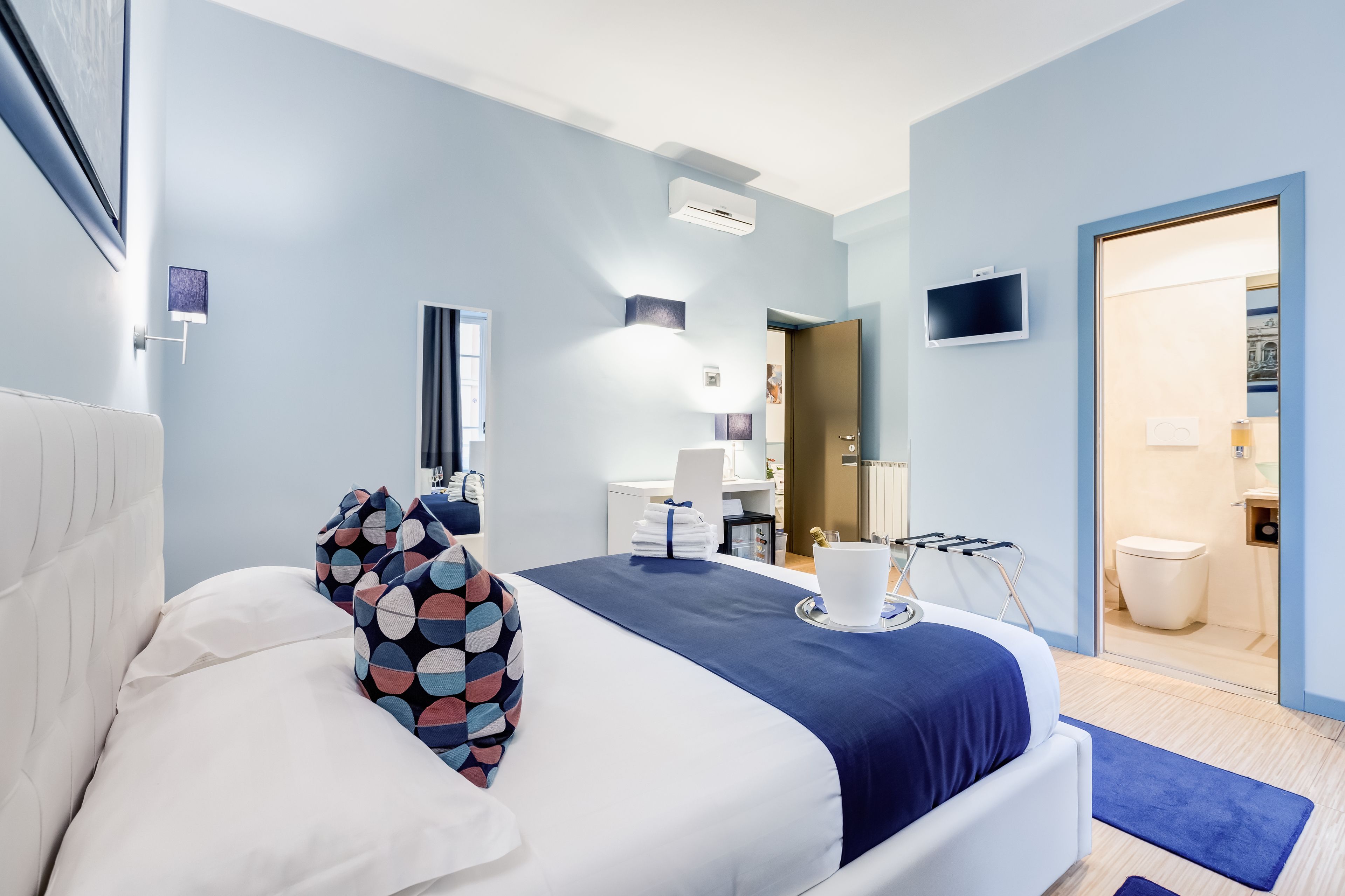 Una habitación de hotel moderna con una cama grande, un televisor de pantalla plana, un escritorio y un baño visible a través de una puerta abierta.