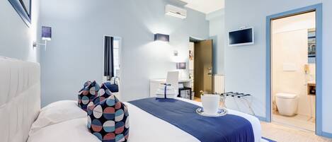 Una habitación de hotel moderna con una cama grande, un televisor de pantalla plana, un escritorio y un baño visible a través de una puerta abierta.