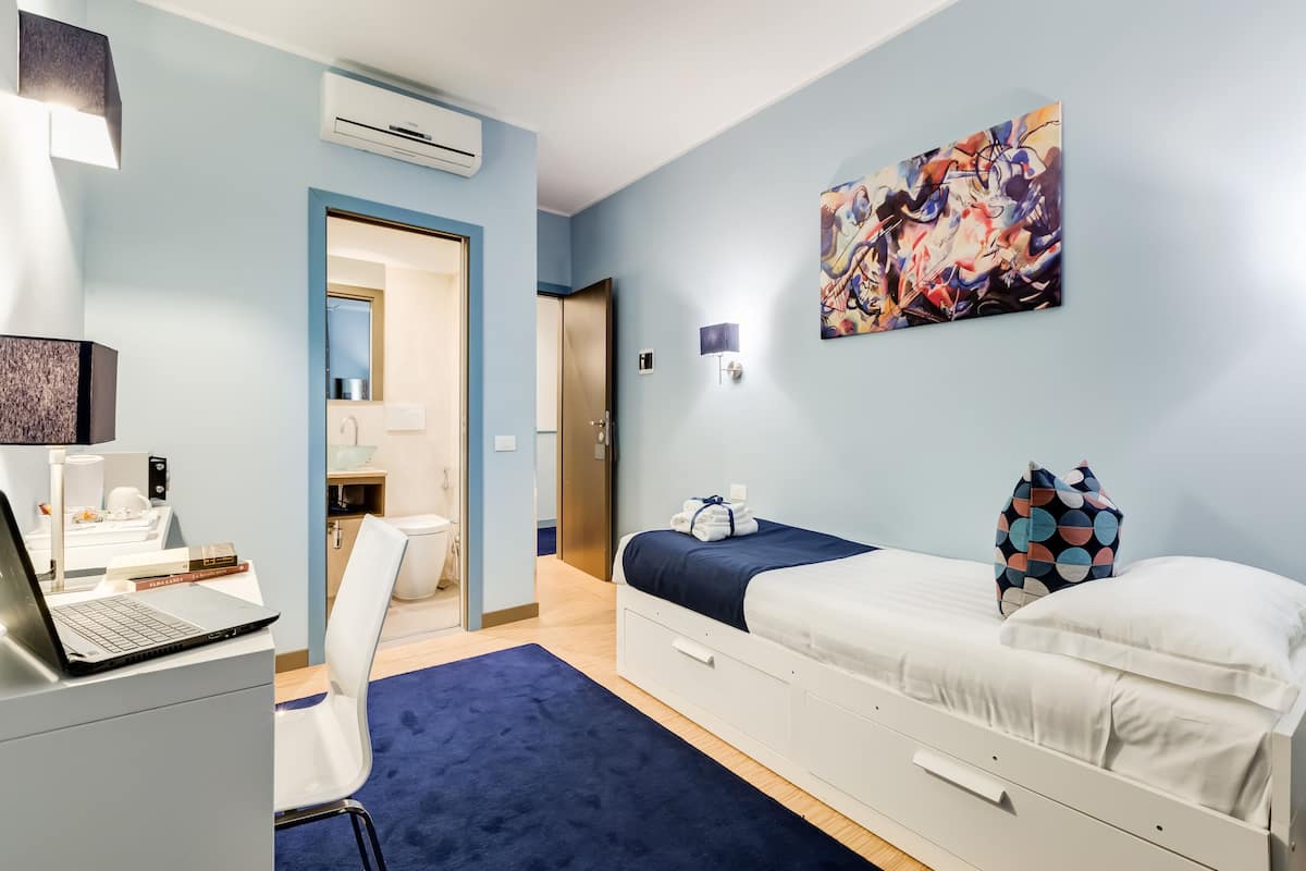 Una habitación de hotel moderna con escritorio, ordenador portátil y cama con colcha azul.
