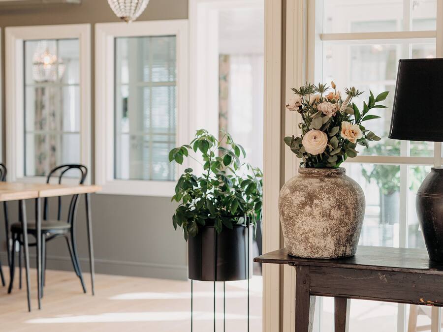 A room with a wooden floor, a table with chairs, a vase with flowers, and a lamp on a side table.