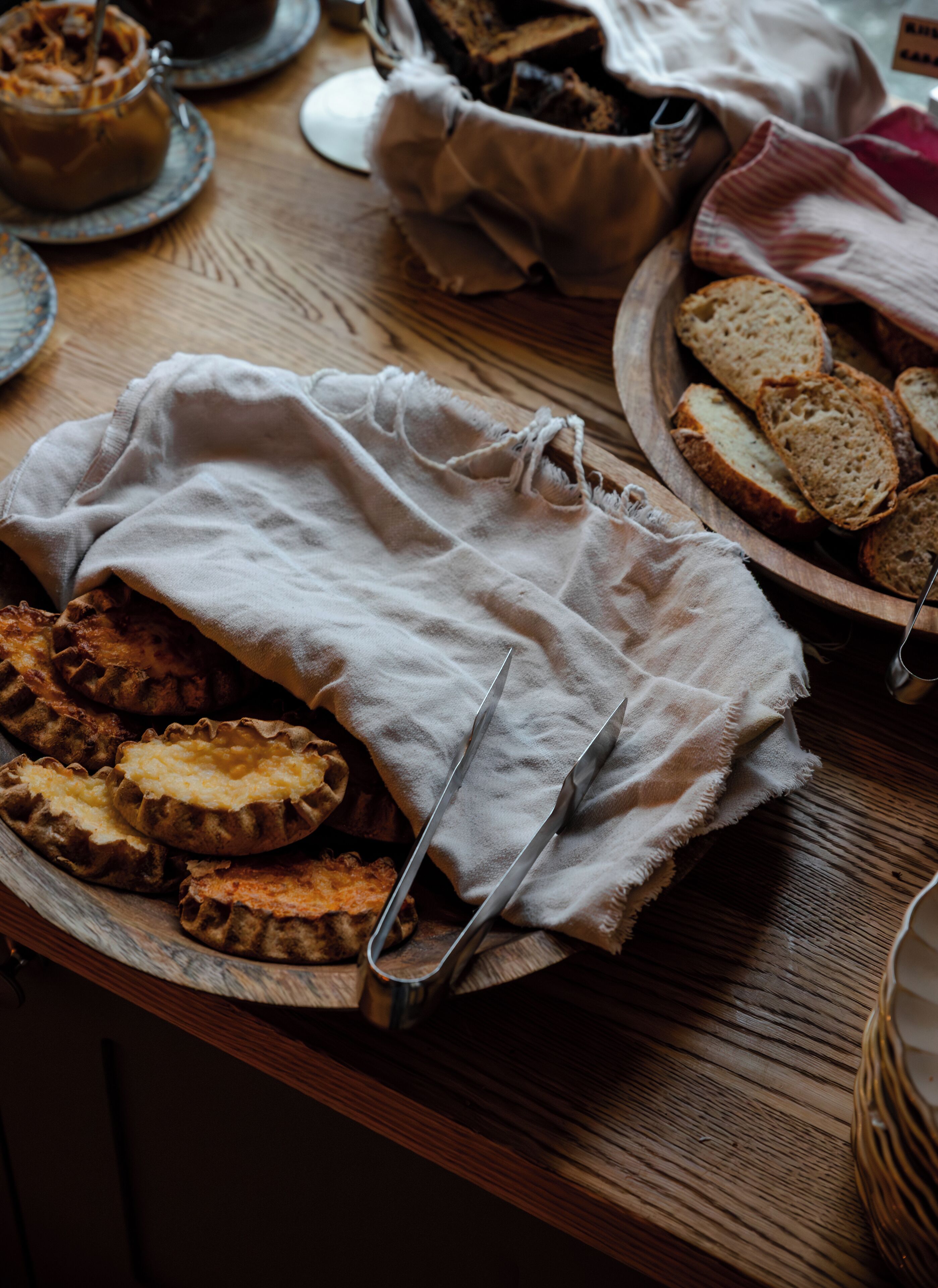 A wooden table with bread, a cloth, and a pair of scissors.