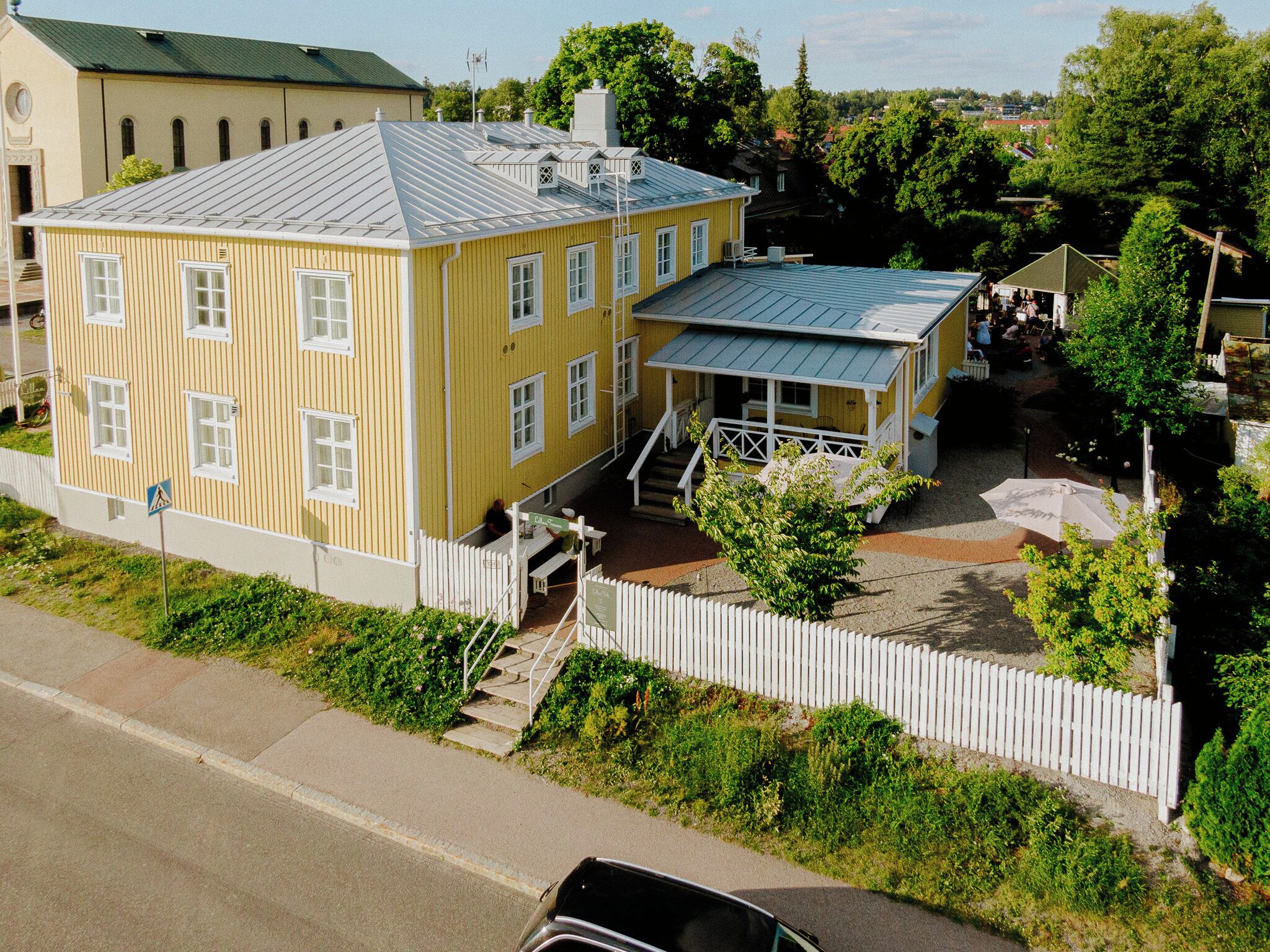 A yellow building with a blue roof, a white fence, and a small porch.