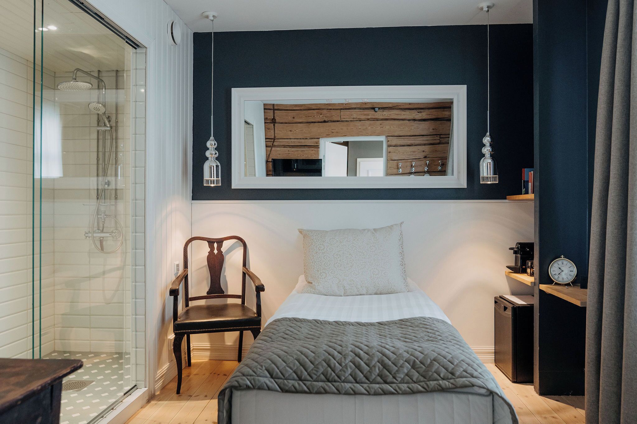 Quarto moderno com cama, cadeira, mesa de cabeceira pequena, relógio e espelho.