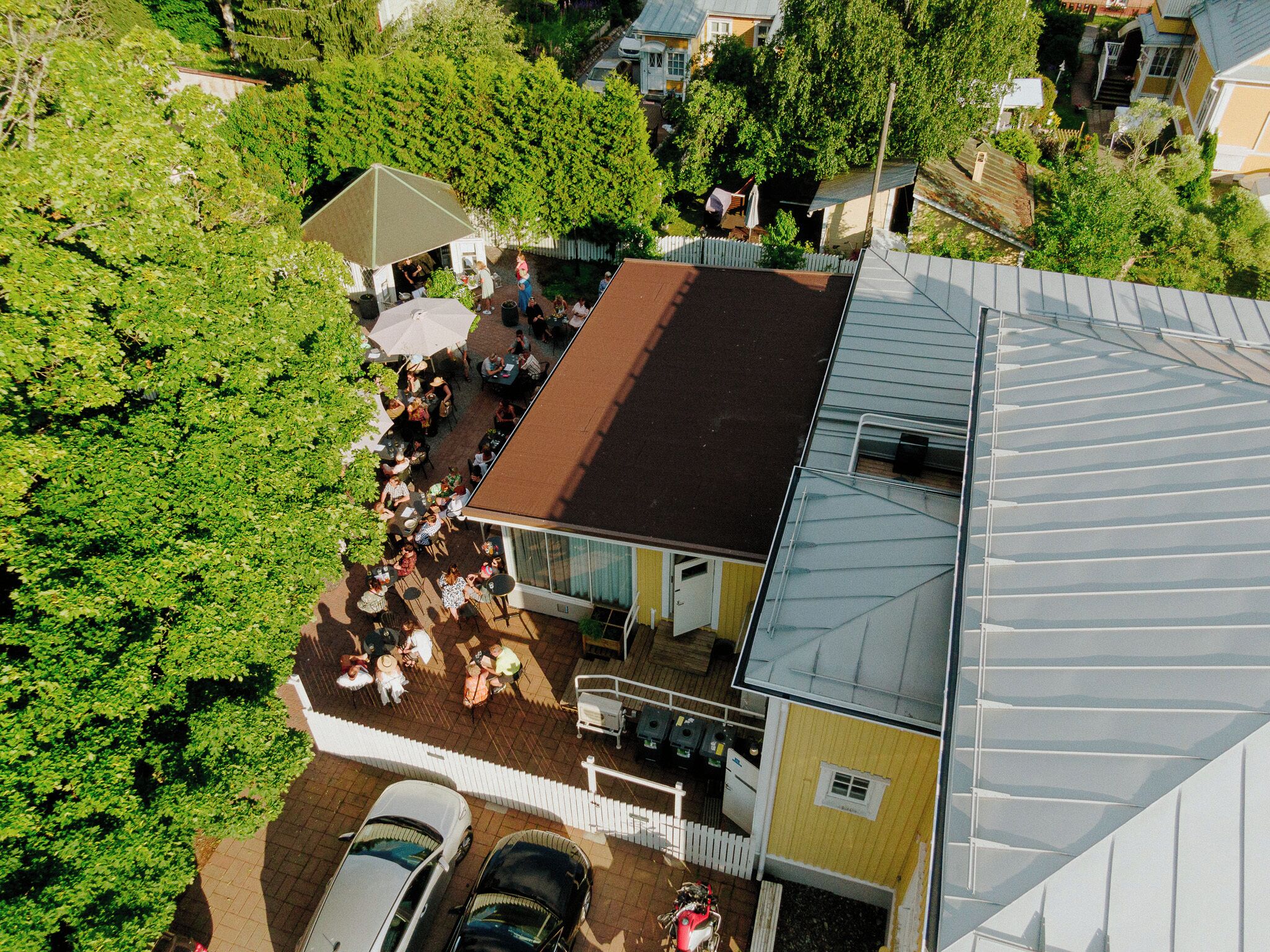 Vista aérea de una zona residencial con una casa de techo inclinado, un patio con mobiliario exterior y un jardín cercado.