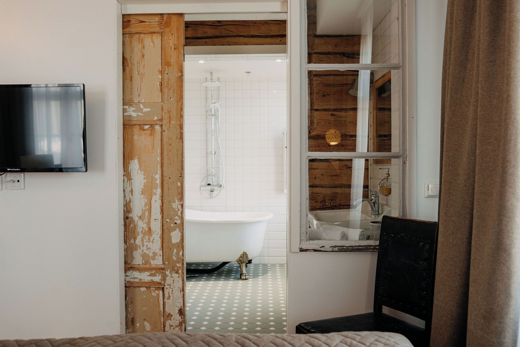 A bathroom with a white bathtub, a wooden door, and a television mounted on the wall.