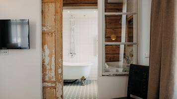 A bathroom with a white bathtub, a wooden door, and a television mounted on the wall.