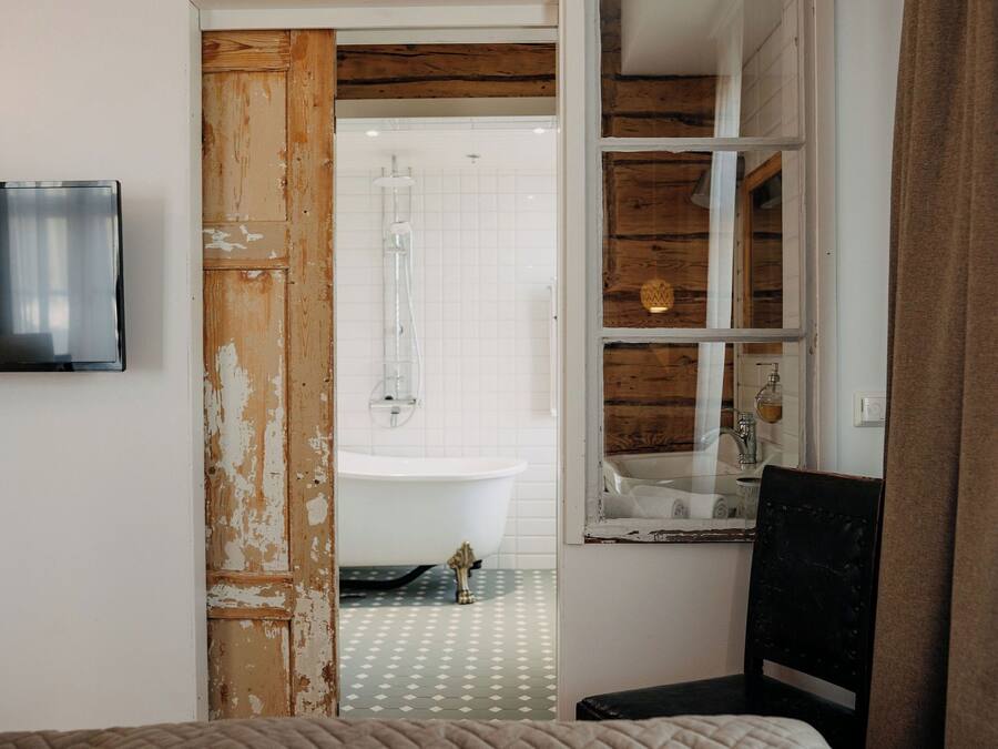 A bathroom with a white bathtub, a wooden door, and a television mounted on the wall.