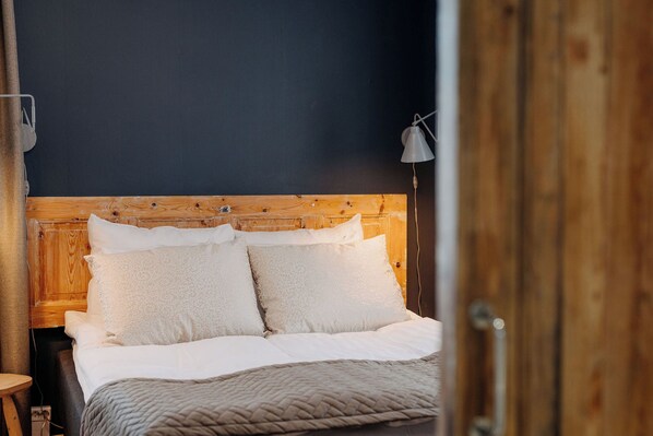 A neatly made bed with white linens and a textured blanket, a wooden headboard, and a bedside lamp. - Lillan Hotel & Kök (Tampere)