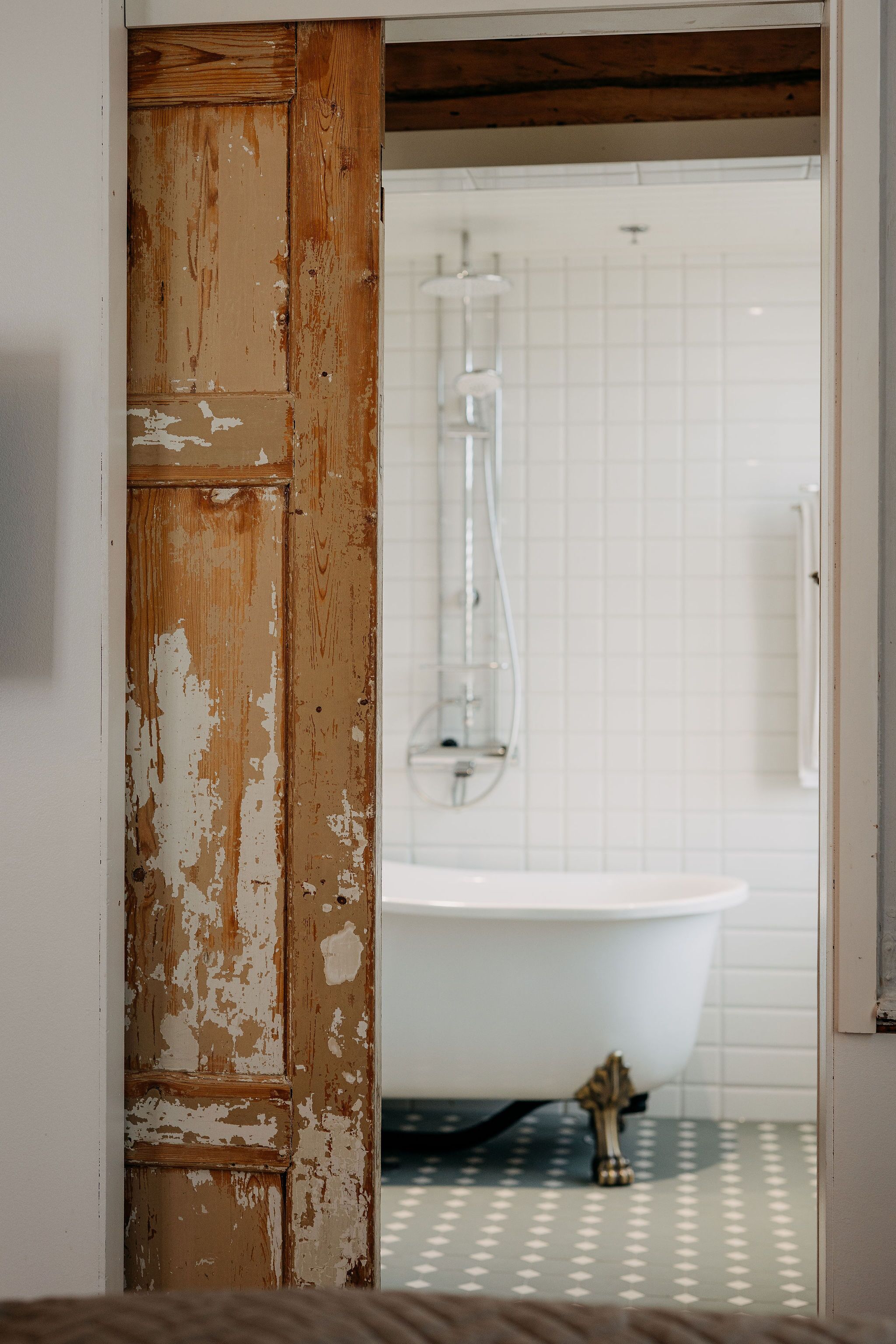 Un baño con una bañera blanca, un box de ducha de vidrio y una puerta de madera desconchada.