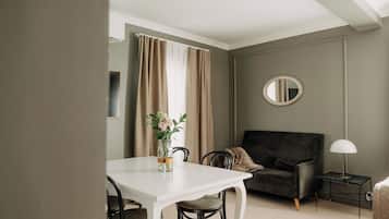 A room with a white dining table, a black sofa, a small side table with a lamp, and a round mirror on the wall.