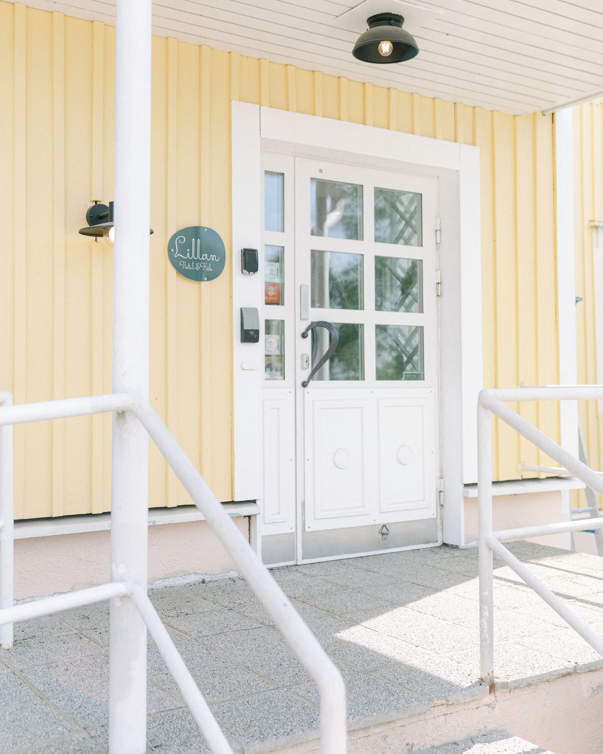 A building with a white door and yellow walls, a sign reading "Lillan Hotel," and a metal railing in front.