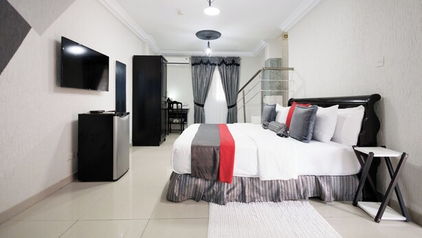 A modern bedroom with a bed, TV, and a staircase. - The Ritzz Exclusive Guest House (Accra)