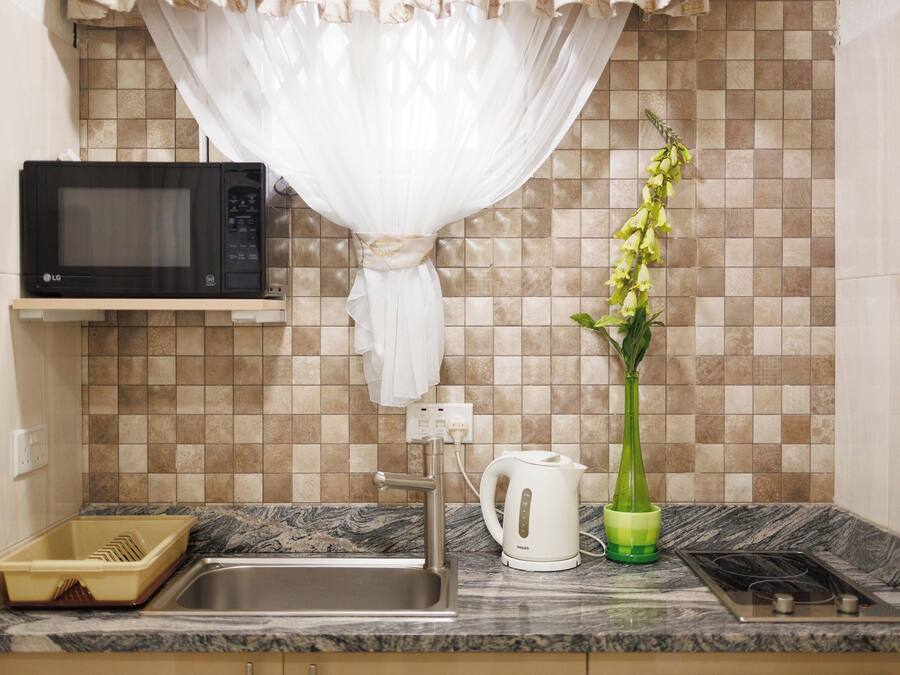 A kitchen with a microwave, sink, kettle, and a vase with a plant.