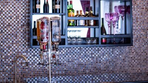 A bar area with a tiled backsplash, a shelf with bottles and glasses, and two pendant lights. - The Ritzz Exclusive Guest House (Accra)