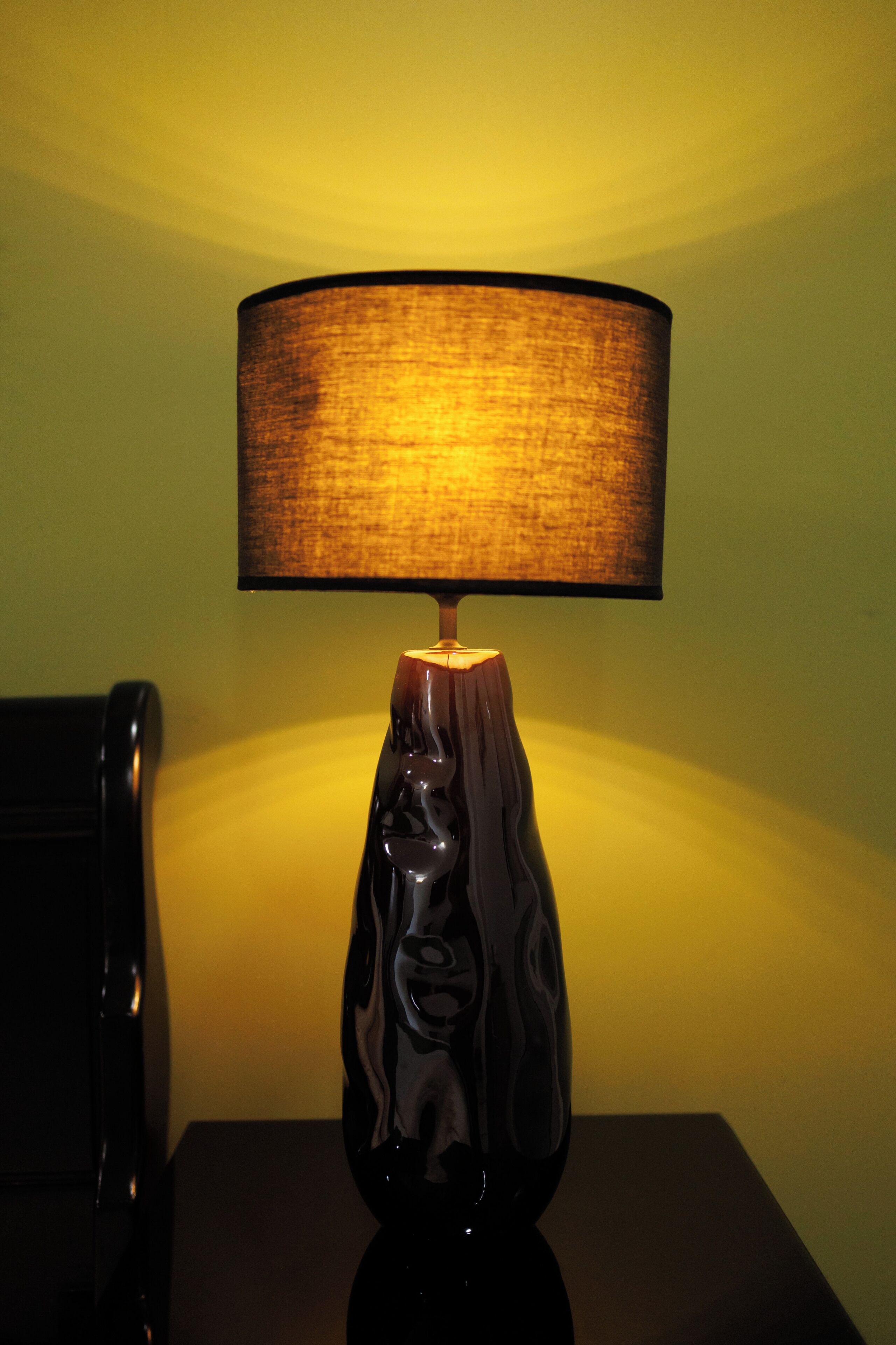 A lamp with a textured shade on a table against a plain wall.
