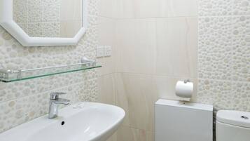 A bathroom with a pedestal sink, a glass shelf, a toilet, and a mirror.