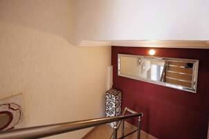 A staircase with a handrail, a mirror on the wall, and a patterned box against the wall.