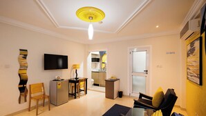 A modern living room with a flat-screen TV, a dining area with a table and chairs, a kitchen in the background, and a door leading to another room. - The Ritzz Exclusive Guest House (Accra)