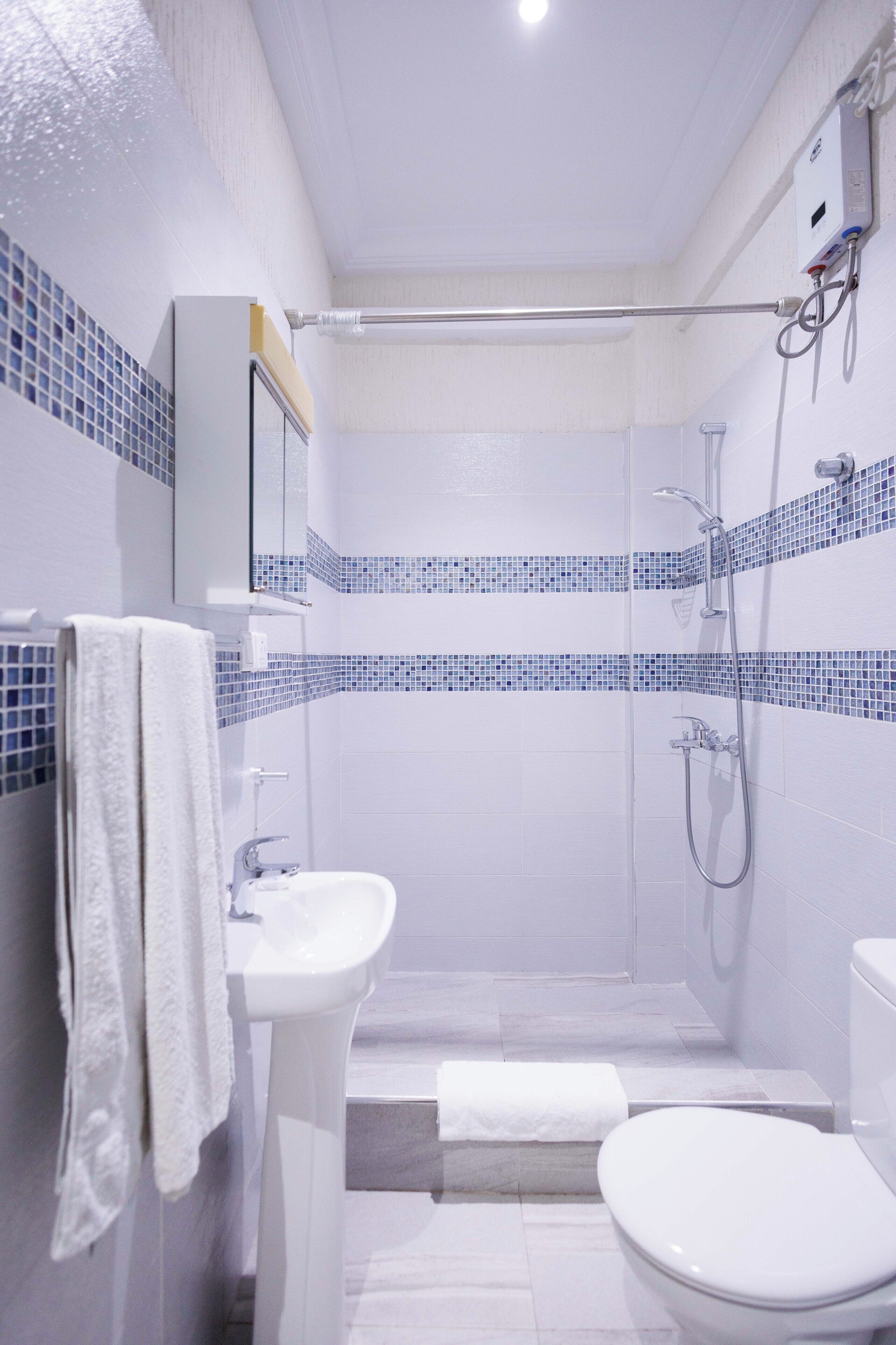 Un baño con ducha, inodoro y lavamanos, con azulejos de mosaico azul en las paredes.
