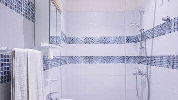 Un baño con ducha, inodoro y lavamanos, con azulejos de mosaico azul en las paredes.