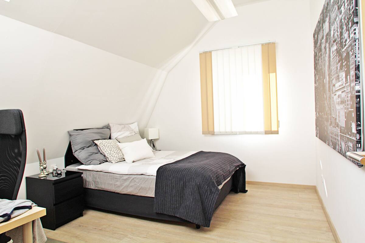 A bedroom with a bed, bedside table, lamp, and a large window.