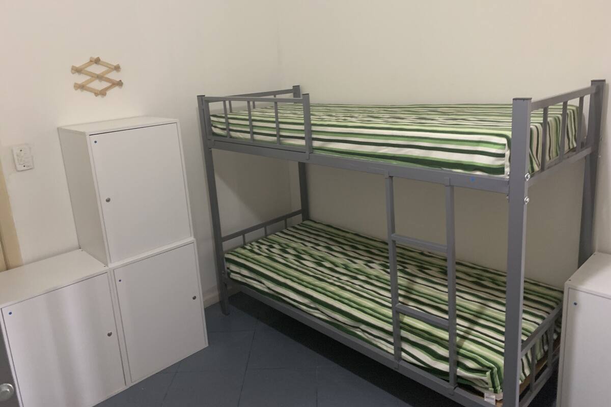 Ein Etagenbett mit grün-weiß gestreifter Bettwäsche, ein weißer Kleiderschrank und ein kleines Regal.