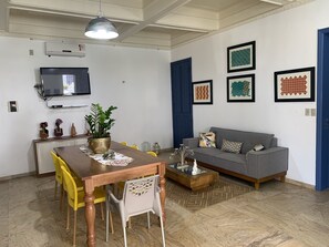 Un salon moderne comprenant un coin repas, un canapé gris et un téléviseur fixé au mur.