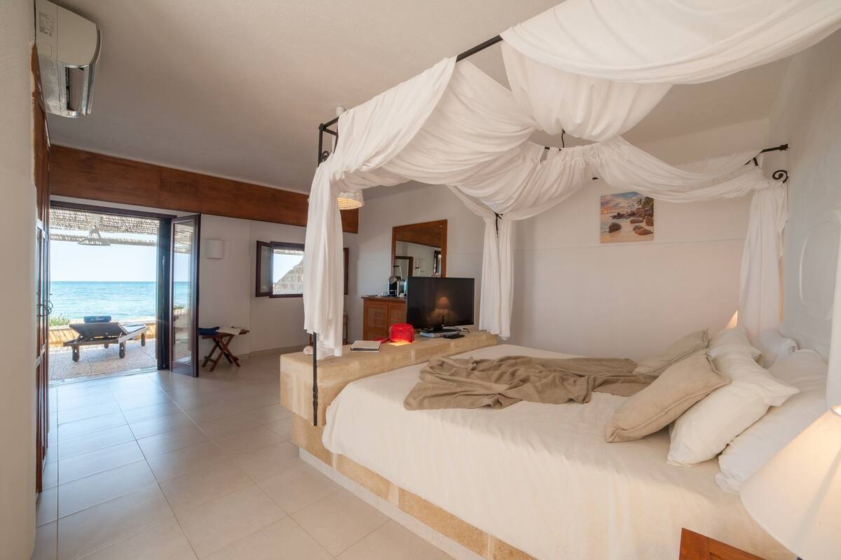 Ein Schlafzimmer mit Himmelsbett, Fernseher und Blick auf den Strand.