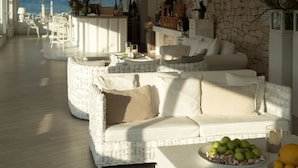 A spacious, sunlit lounge area with wicker furniture, a dining table with fruits, and a view of the sea. - La Peschiera (Monopoli)