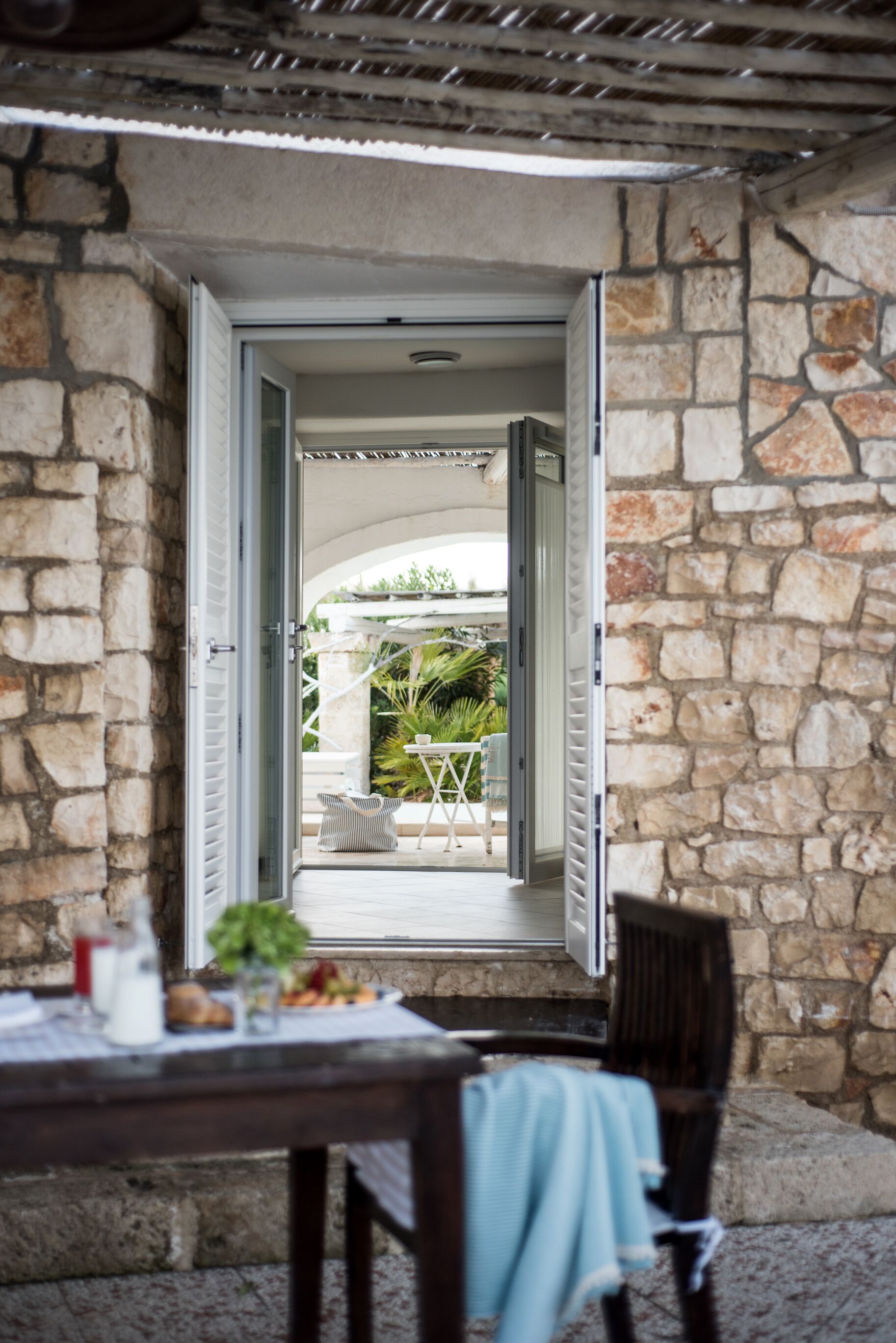 An open doorway leading to a patio area with a table and chairs, surrounded by stone walls.