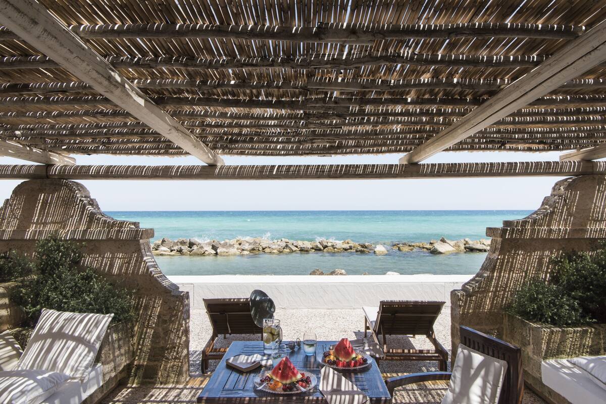 Ein Sitzbereich im Freien mit Blick auf das Meer, inklusive Tisch mit Speisen und einem Getränk.