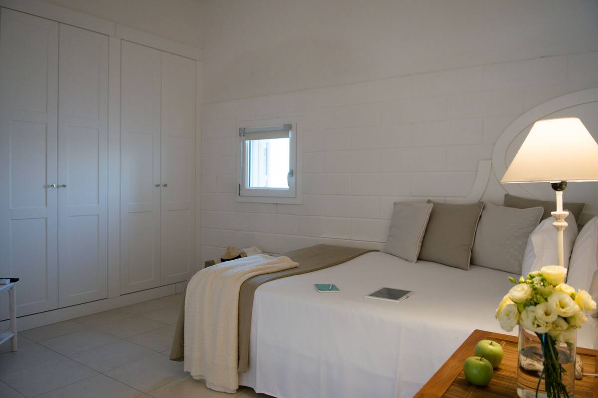 Ein Schlafzimmer mit einem Bett, einem Nachttisch mit Lampe, einem Fenster und einem Kleiderschrank.