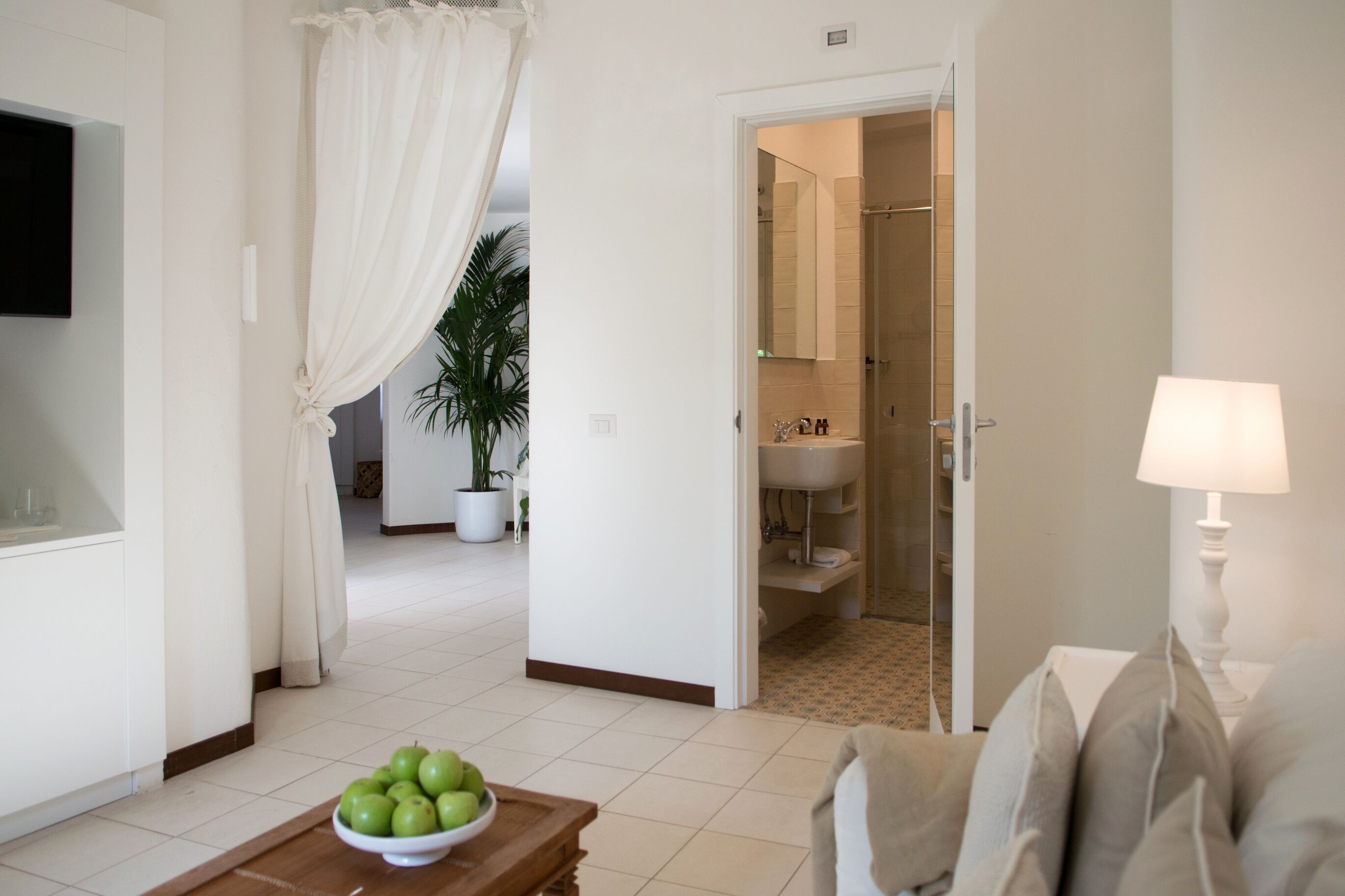 Una sala de estar moderna con una televisión, un tazón de manzanas verdes sobre una mesa de madera y un sofá con almohadones.