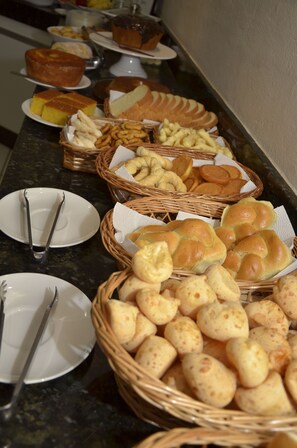 A buffet table with various baked goods including bread, rolls, and pastries. - Hotel Brasil (Guanhaes)