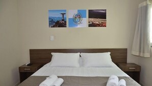 Una habitación de hotel con una cama grande, dos mesitas de noche y tres cuadros en la pared.