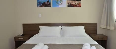 A hotel room with a large bed, two nightstands, and three framed pictures on the wall.