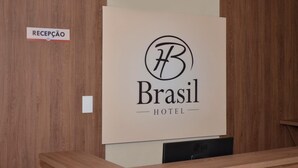 Un mostrador de recepción con un cartel que dice 'RECEPCAO' y un gran cartel de 'Brasil HOTEL' con un logotipo.