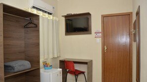 Una habitación pequeña con un armario de madera, un escritorio con una silla, un televisor en la pared y una puerta.