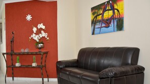 Una sala de estar con un sofá de cuero marrón, una pared de acento roja, una mesita con objetos decorativos y un cuadro de colores en la pared.