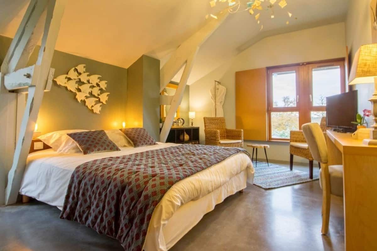 A bedroom with a large bed, a desk, and a chair. There is a window with a view of trees.