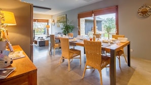 A dining area with a wooden table and wicker chairs, a lamp, and a clock on the wall.