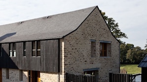 A stone building with a sloped roof, a wooden door, and a fenced outdoor area with a table and chairs.