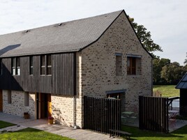 Un edificio de piedra con techo inclinado, una puerta de madera y un espacio exterior amurallado con una mesa y sillas.