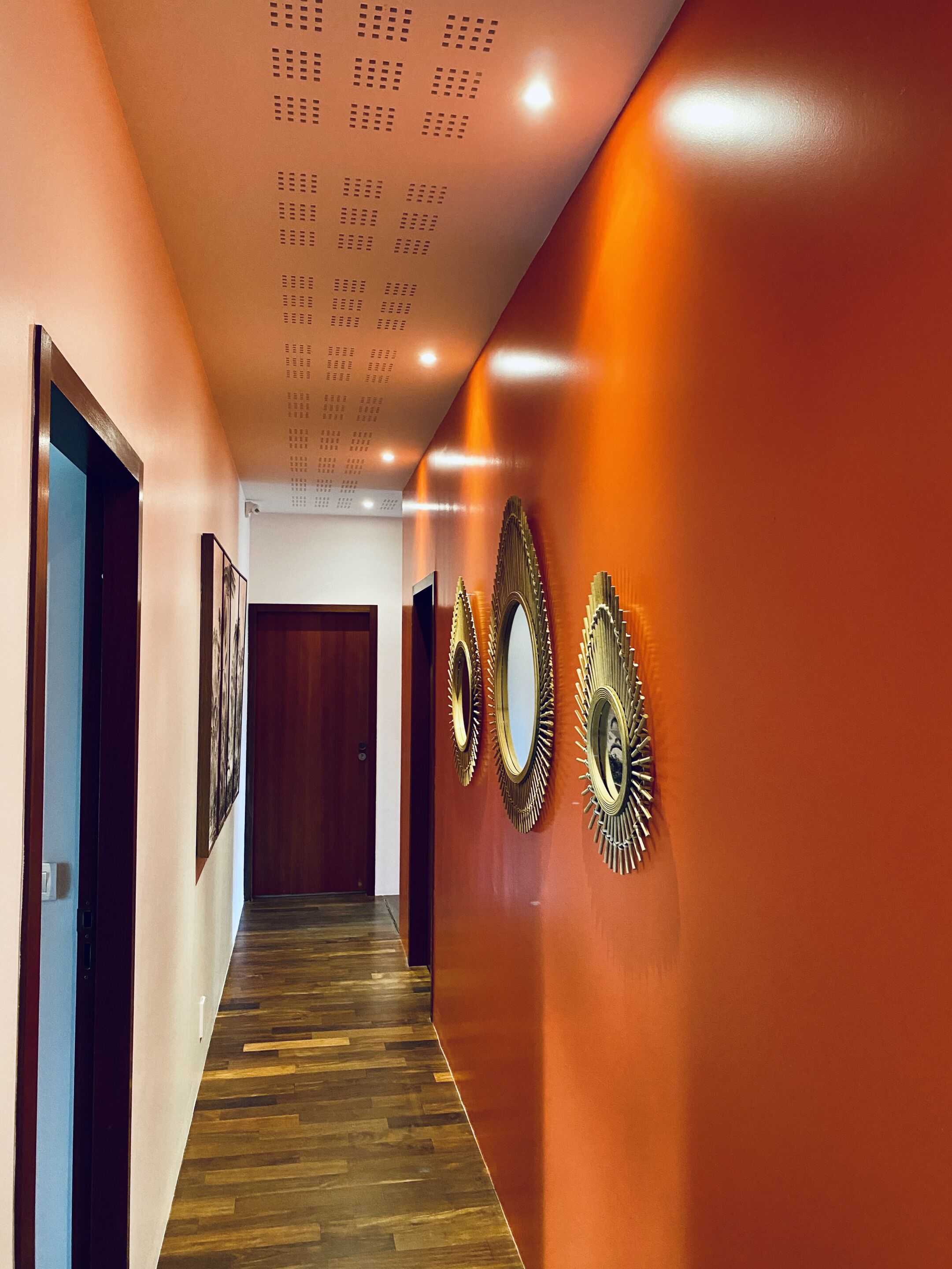 Un pasillo con suelo de madera, pared roja y tres espejos decorativos.