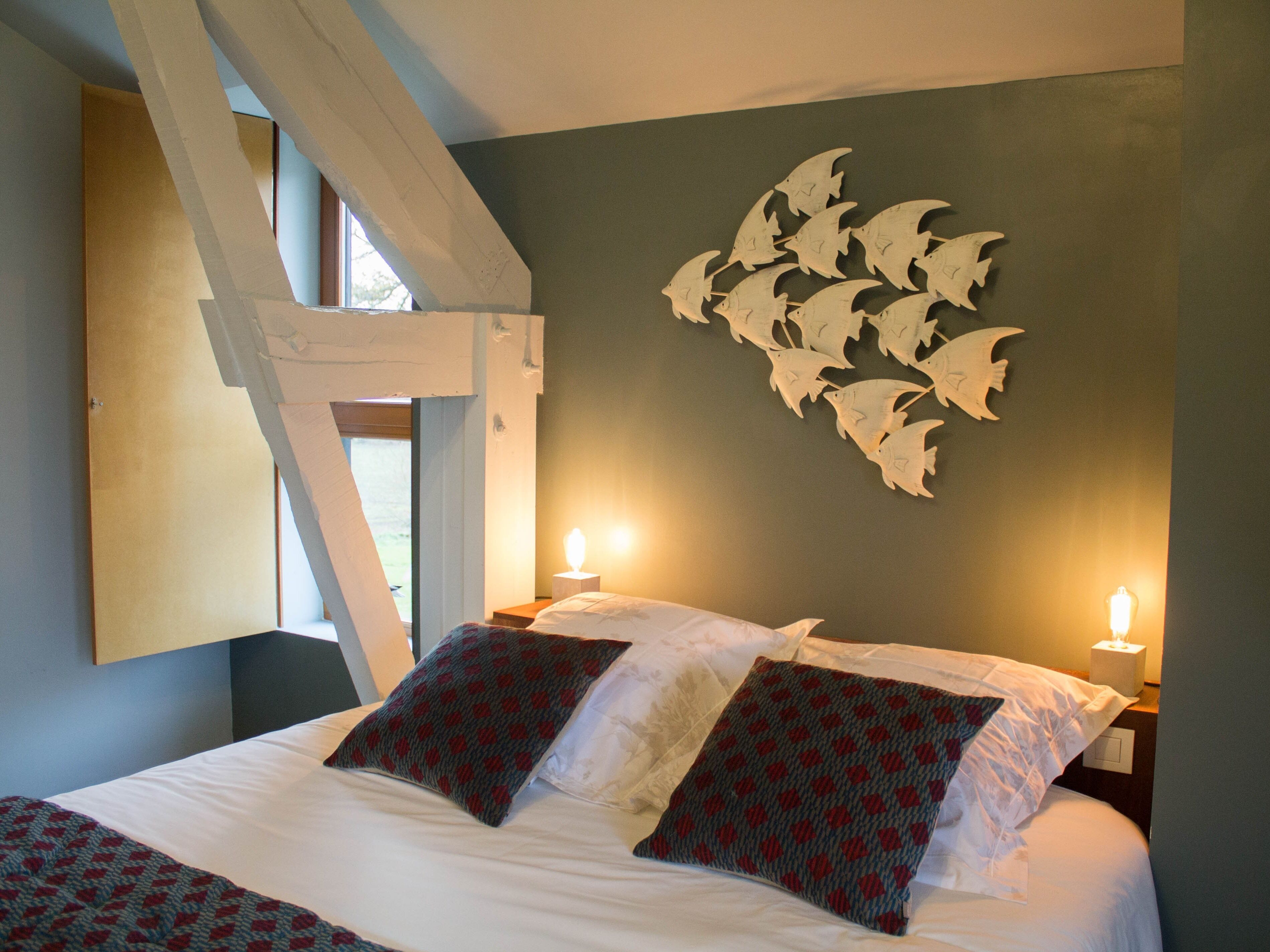 Ein Schlafzimmer mit einem Bett, zwei Kissen, einer Wandleuchte und einem Fenster.