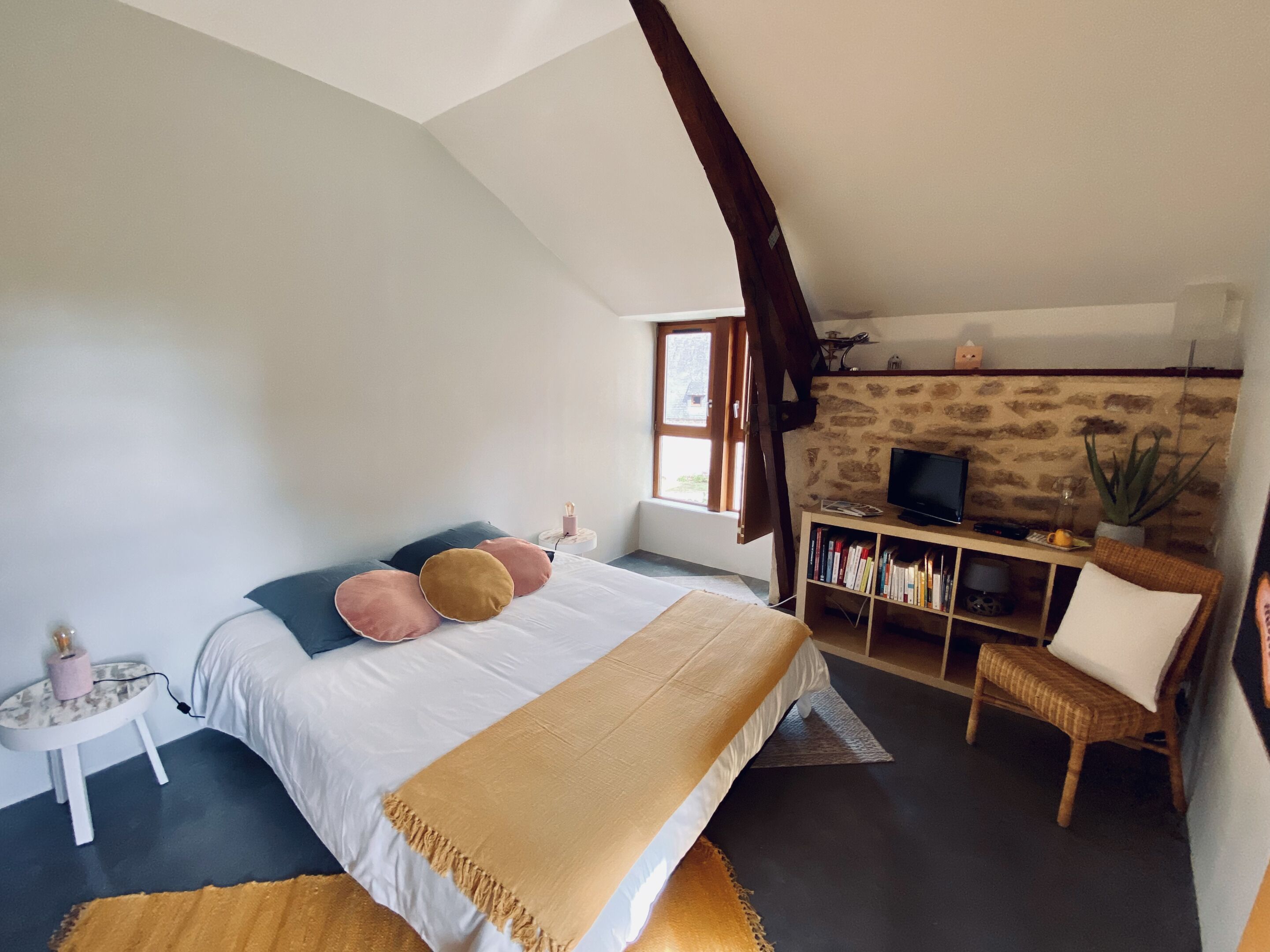 Um quarto com uma cama, uma televisão, uma estante e uma janela.