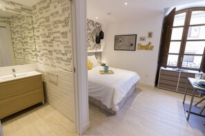 A modern bedroom with a large bed, a bedside table, a desk, and a bathroom with a mirror and sink. - Besalamanca (Salamanca)