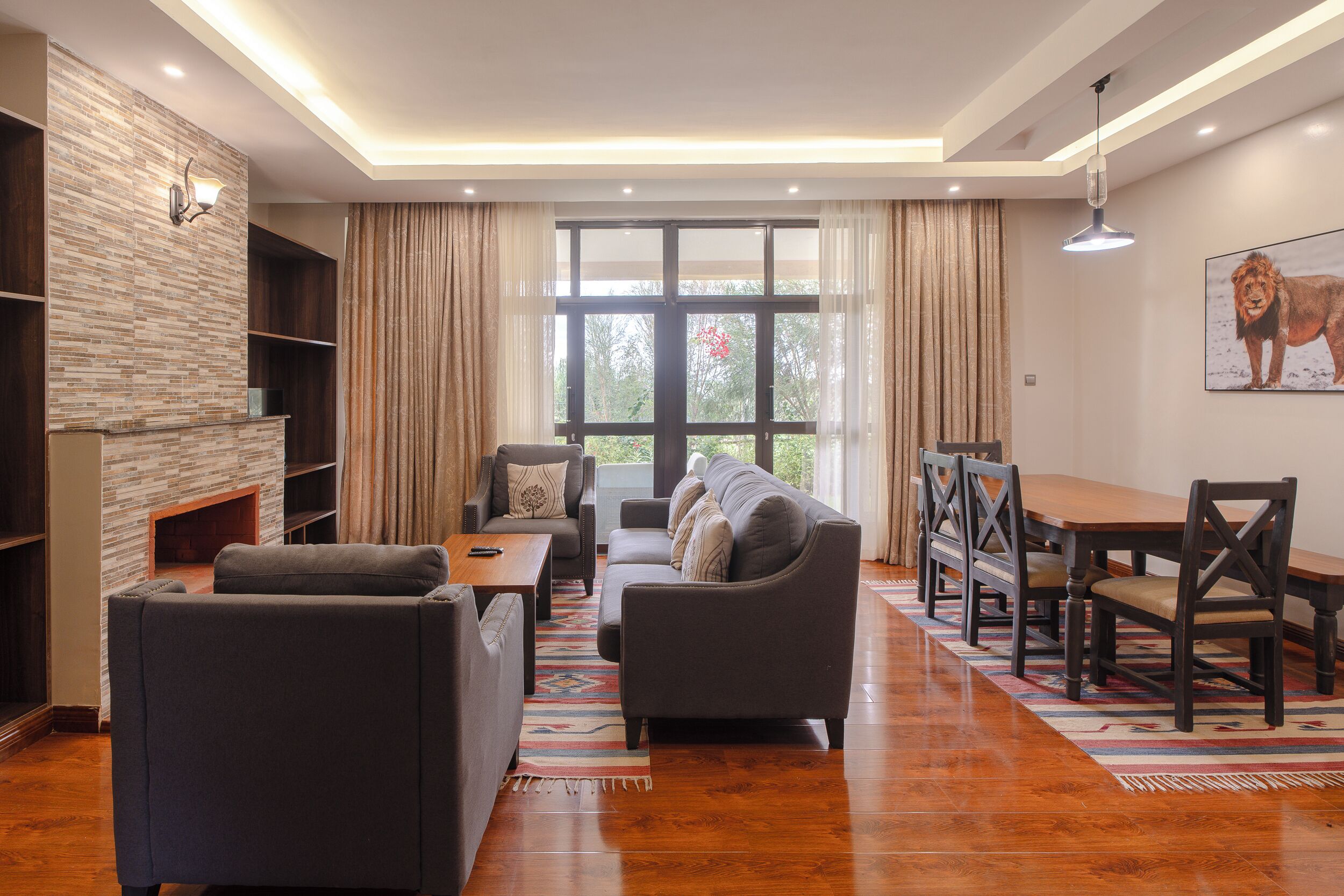 A modern living room with a fireplace, a sofa, a dining table with chairs, and a large window with curtains.