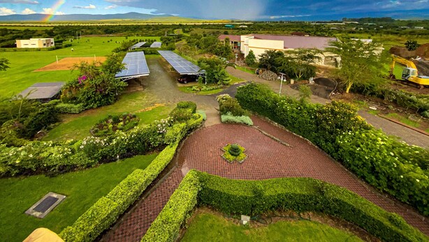 A landscaped area with solar panels, a paved walkway, and a view of distant buildings under a partly cloudy sky with a rainbow. - Maiyan Luxury Resort (Nanyuki)